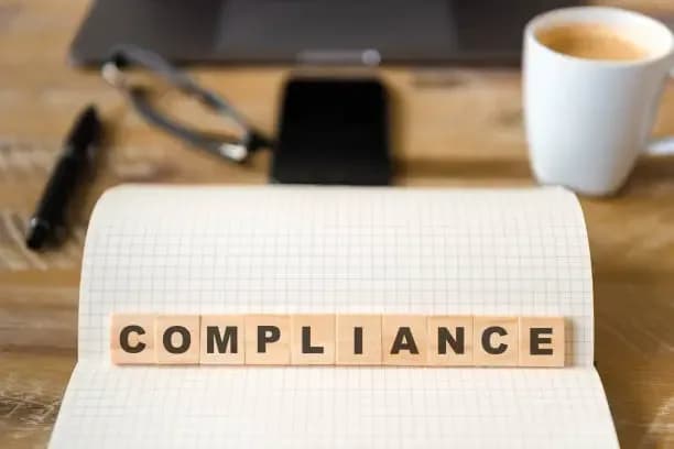 The word compliance spelled in wooden letter tiles on an open notebook
